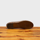 Outsole of Taupe woven flat shoe on a wooden surface with a light gray background