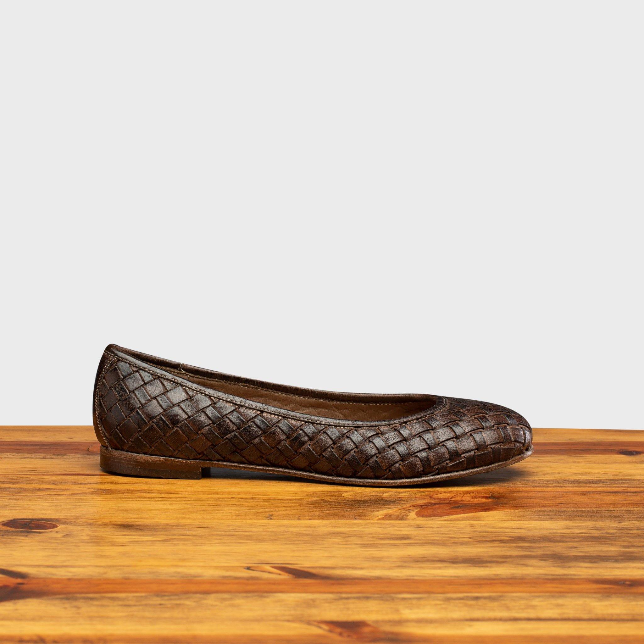 Tobacco woven flat shoe on a wooden surface with a light gray background
