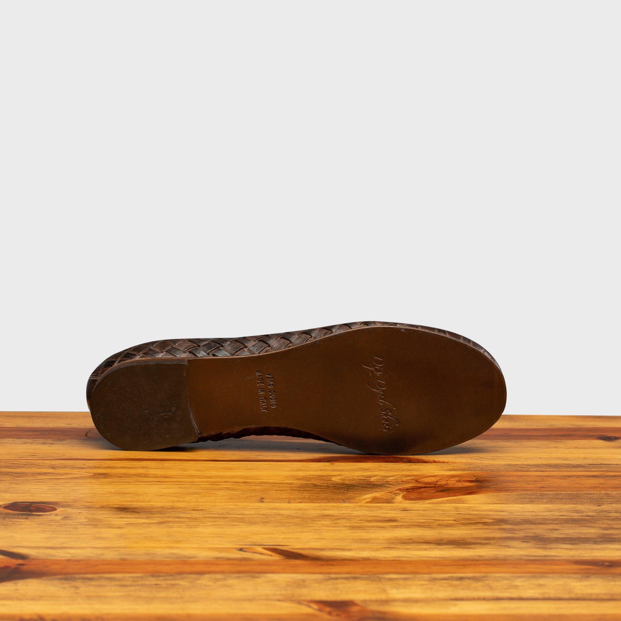 Outsole of Tobacco woven flat shoe on a wooden surface with a light gray background