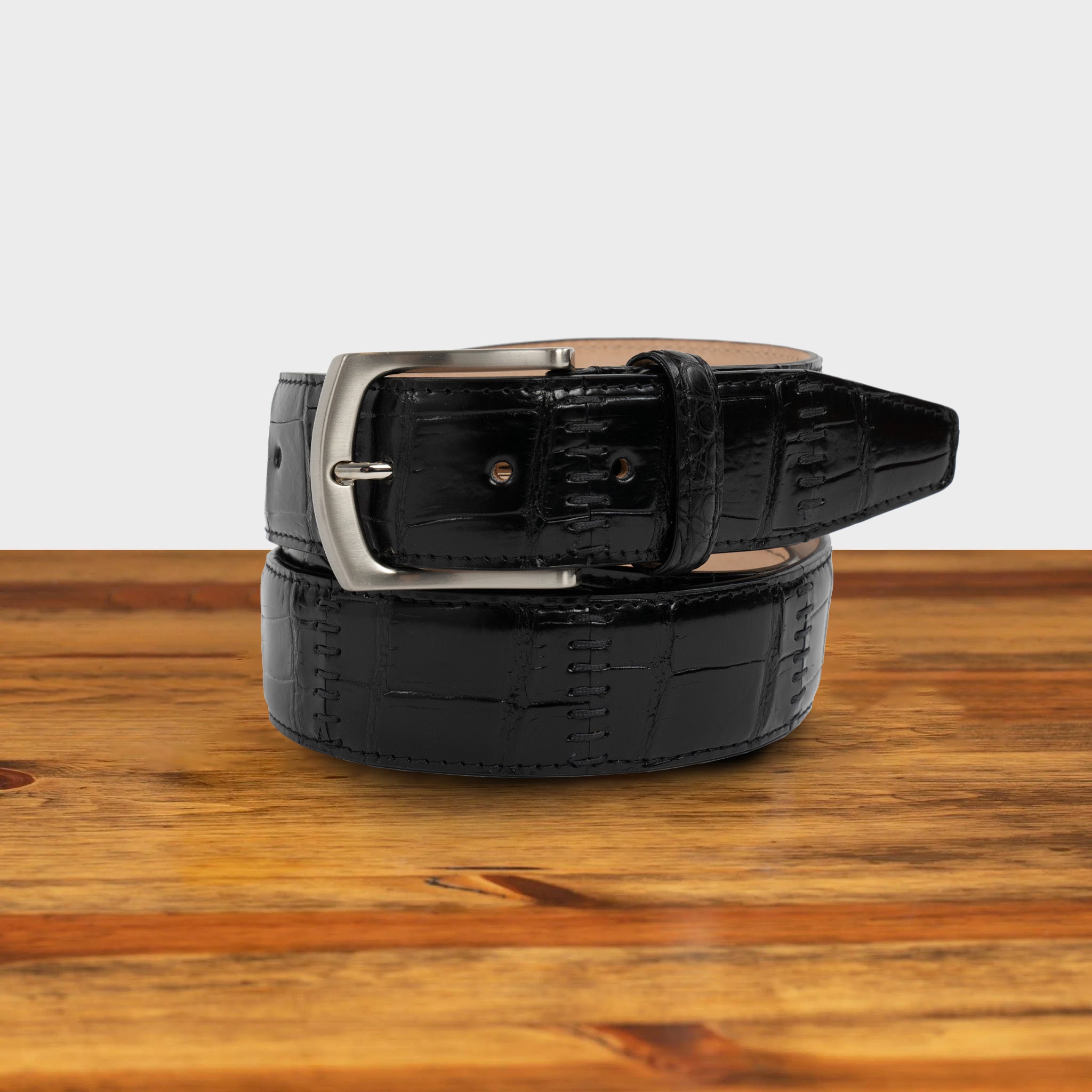 Black textured belt with a silver buckle on a wooden surface