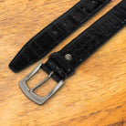 Black textured belt with a silver buckle on a wooden surface