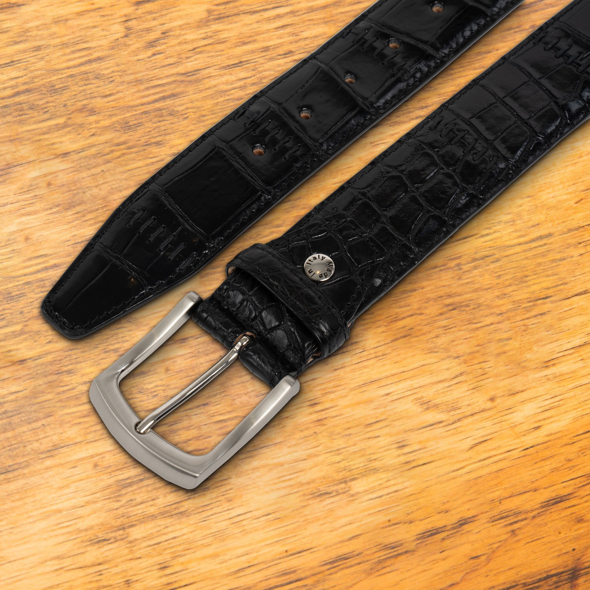 Black textured belt with a silver buckle on a wooden surface