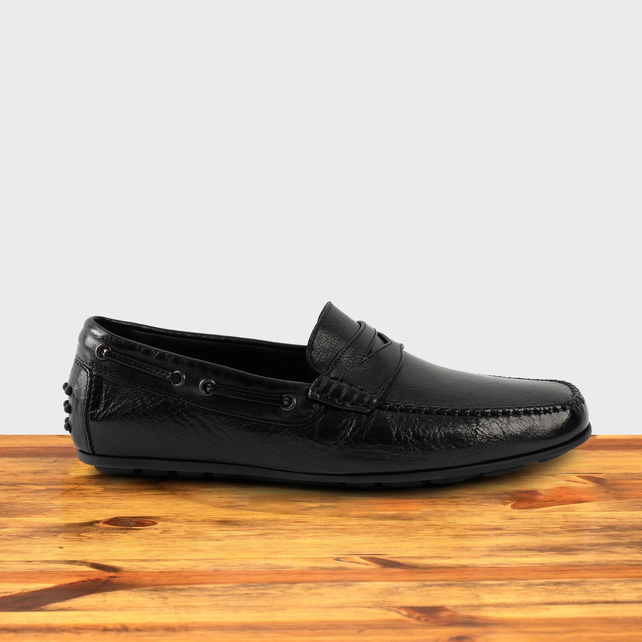 Black leather loafer on a wooden surface with a white background