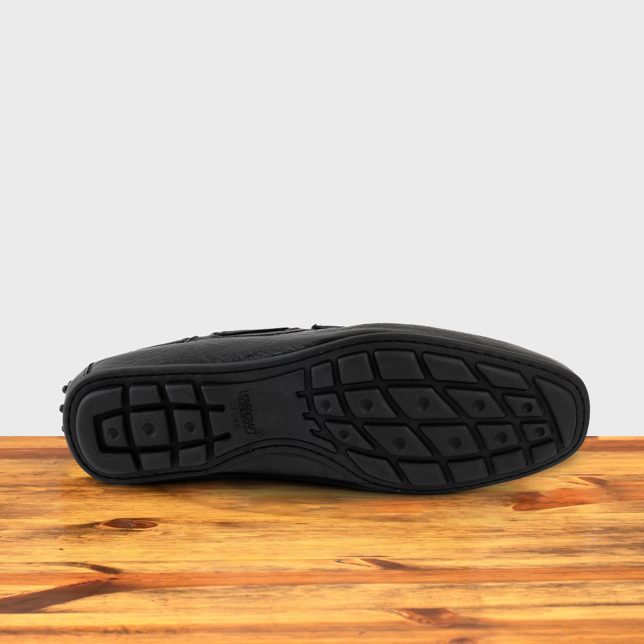 Outsole of Black leather loafer on a wooden surface with a white background