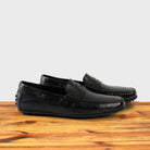 A Pair of Black leather loafer on a wooden surface with a white background