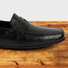 Black leather loafer on a wooden surface with a white background