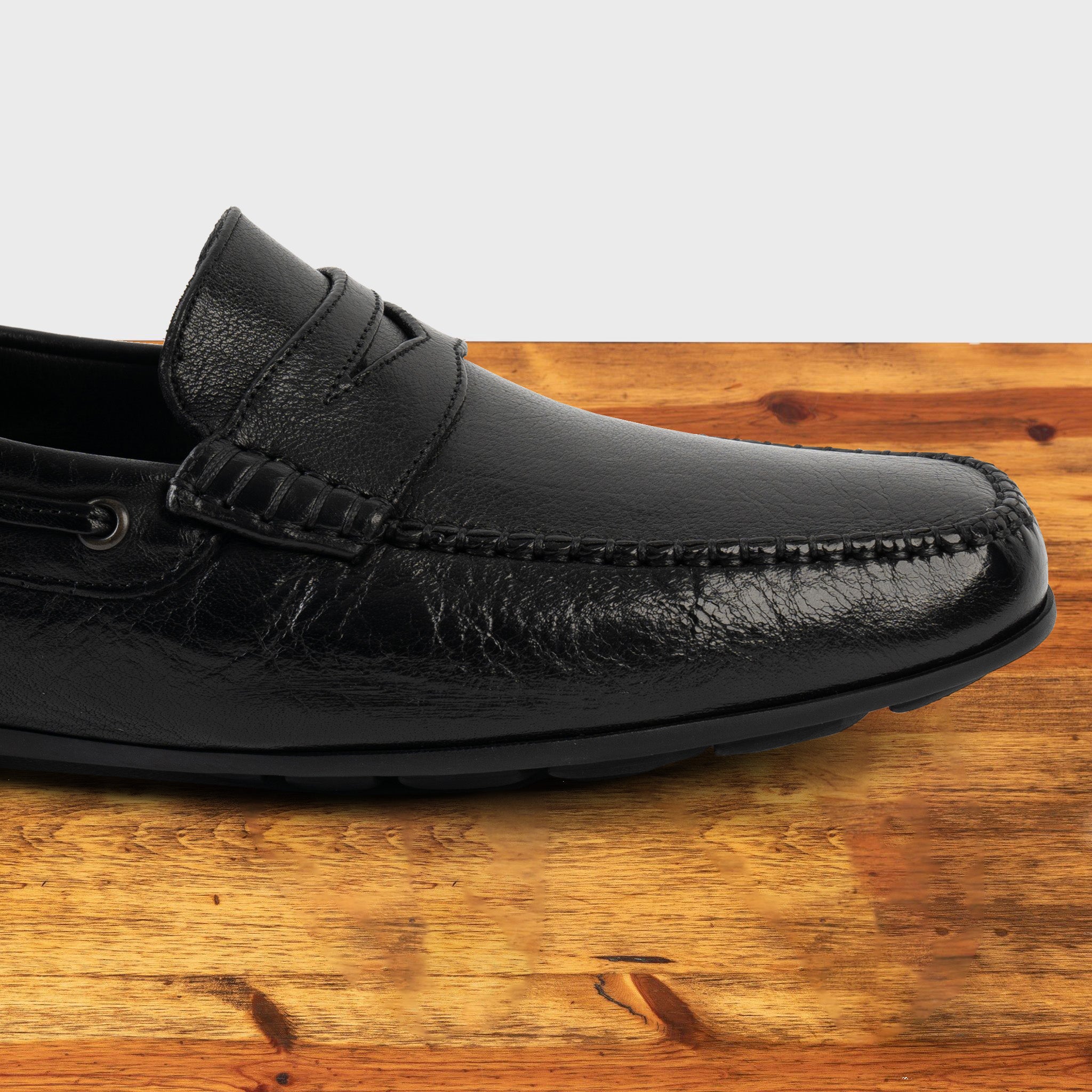 Black leather loafer on a wooden surface with a white background