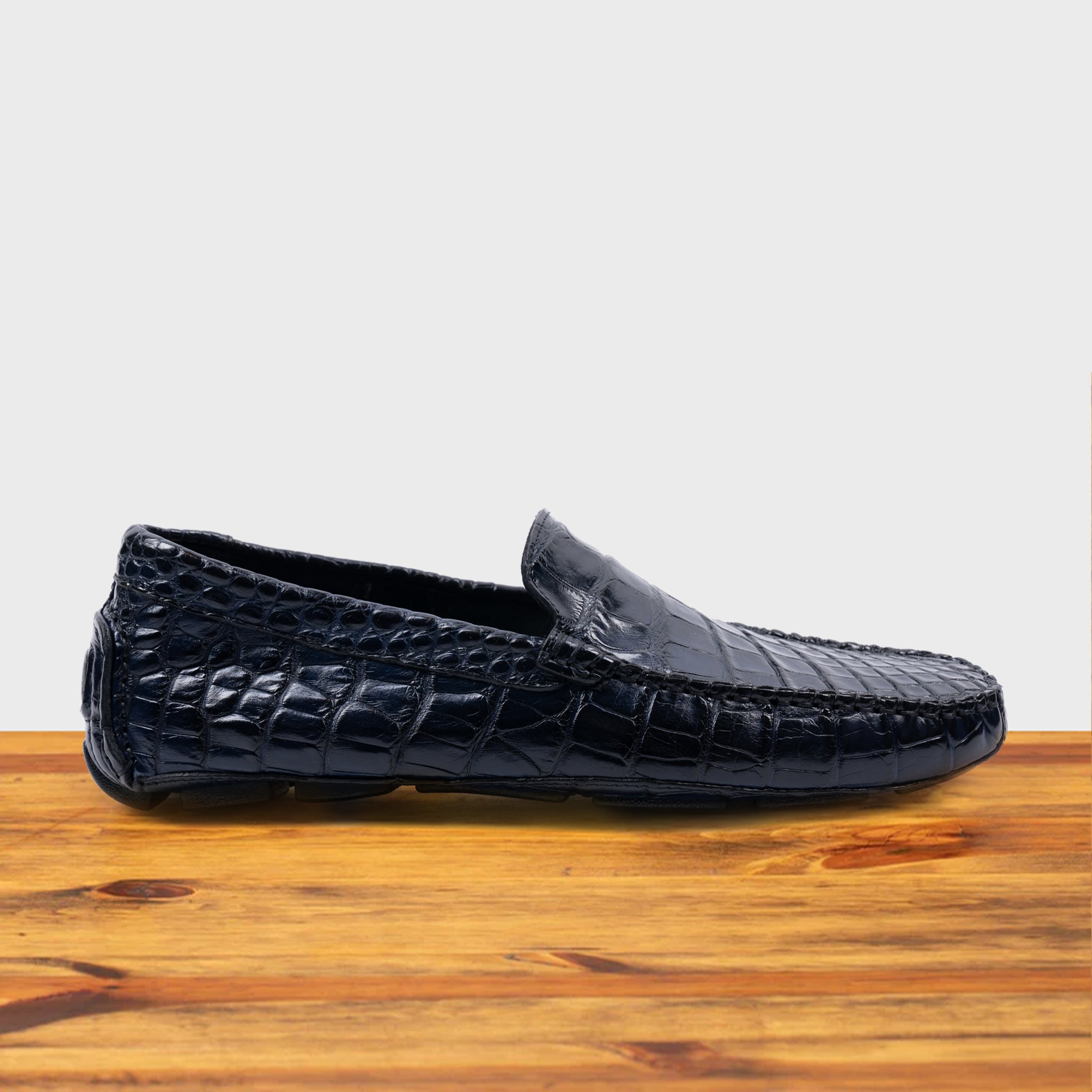 Blue crocodile-patterned loafer on a wooden surface with a light gray background