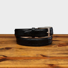 Black leather belt with a silver buckle on a wooden surface