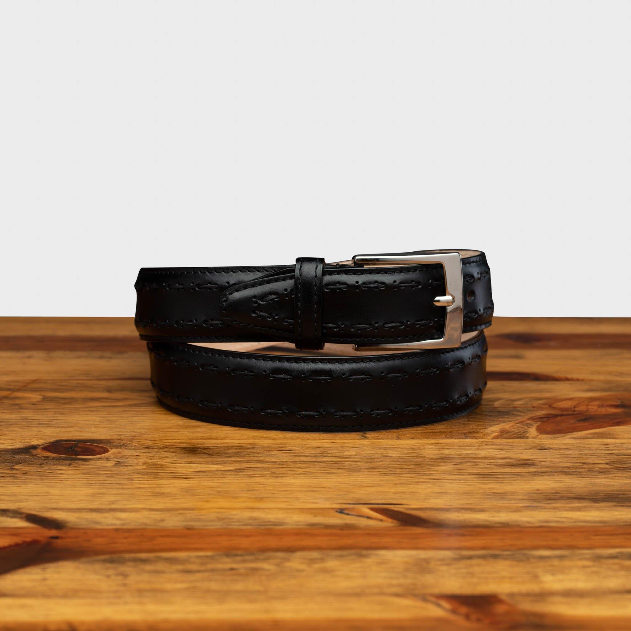 Black leather belt with a silver buckle on a wooden surface