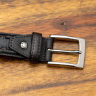Black leather belt with a silver buckle on a wooden surface