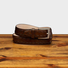 Mahogany leather belt with a silver buckle on a wooden surface