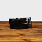 Black leather belt with silver buckle on a wooden surface