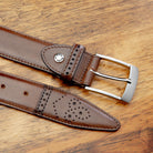 Brown leather belt with silver buckle on a wooden surface
