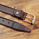 Burgundy leather belt with silver buckle on a wooden surface