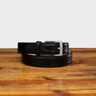 Black leather belt with a silver buckle on a wooden surface