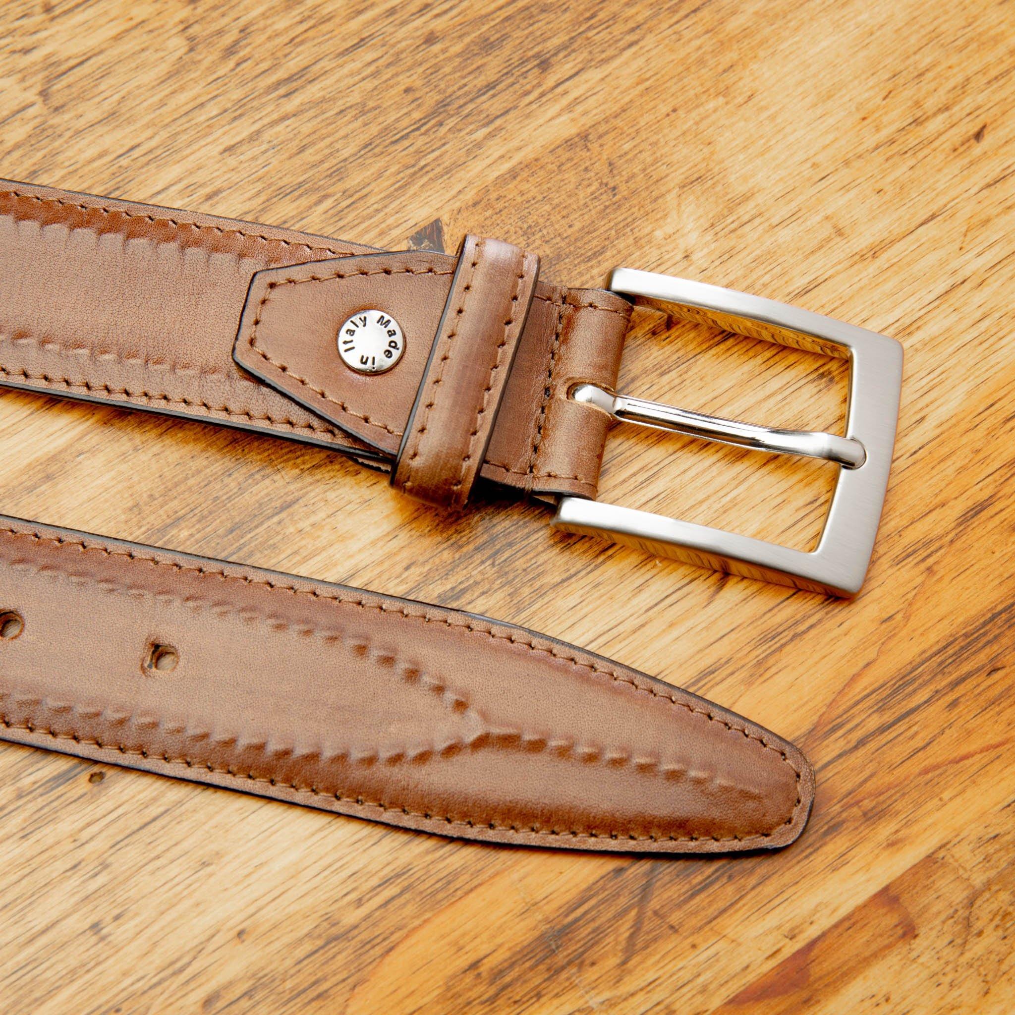 Caramel leather belt with a silver buckle on a wooden surface