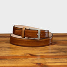 Caramel leather belt with a silver buckle on a wooden surface
