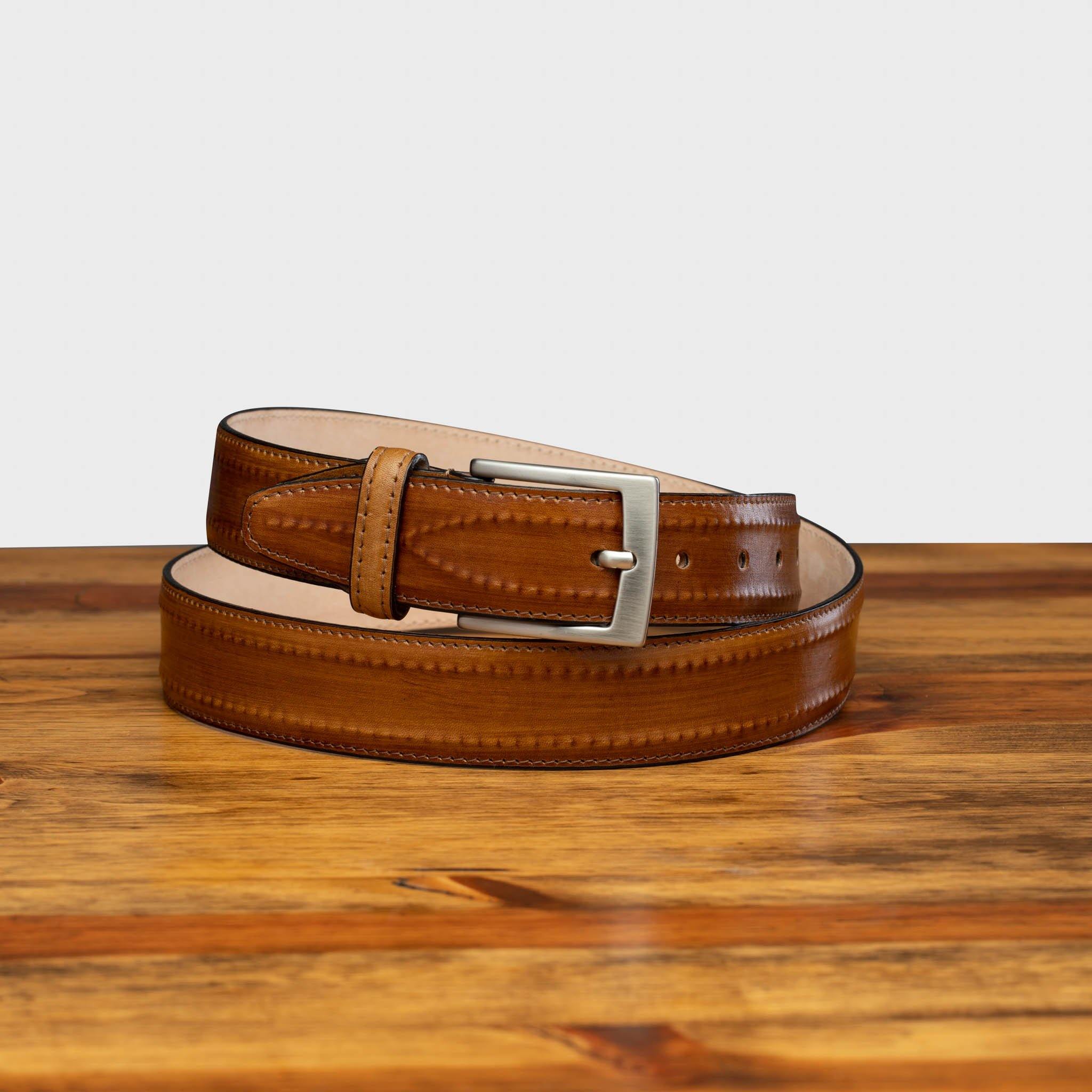Caramel leather belt with a silver buckle on a wooden surface