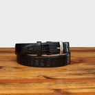 A black genuine exotic hornback belt with a silver buckle on a wooden surface.