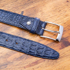 A navy blue genuine exotic hornback belt with a silver buckle on a wooden surface.