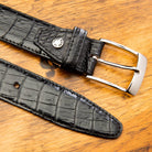 A black genuine exotic hornback belt with a silver buckle on a wooden surface.