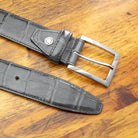 C8099 Gray crocodile leather belt with a polished silver buckle, coiled on a wooden surface