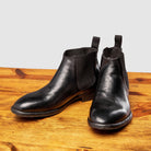 Pair of black leather Chelsea boots on a wooden surface with a light gray background