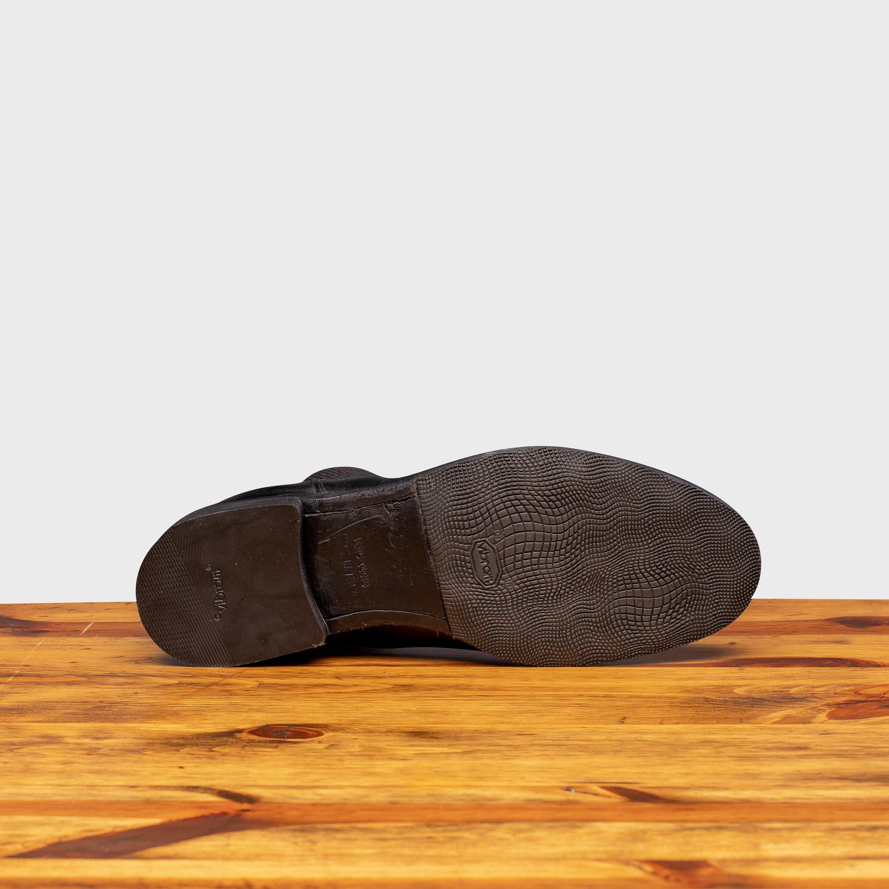 Outsole of black leather Chelsea boots on a wooden surface with a light gray background