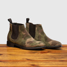 Pair of Camouflage-patterned boot on a wooden surface with a light gray background