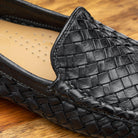 Close-up Black loafer shoe with woven pattern on a wooden surface
