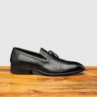 Black leather loafer shoe on a wooden surface with a light gray background