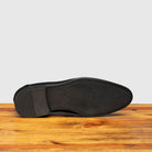 Outsole of black leather loafer shoe on a wooden surface with a light gray background