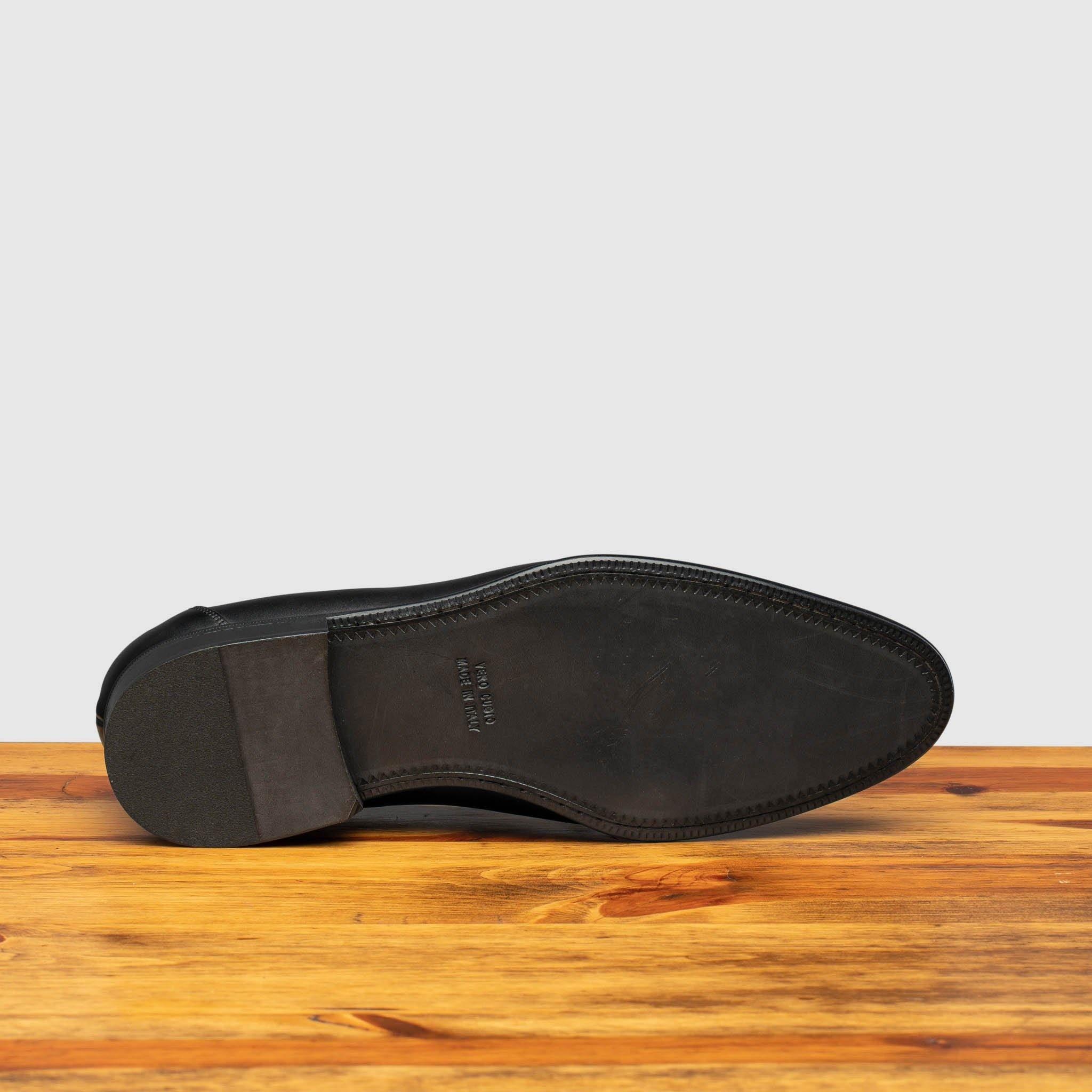 Outsole of black leather loafer shoe on a wooden surface with a light gray background