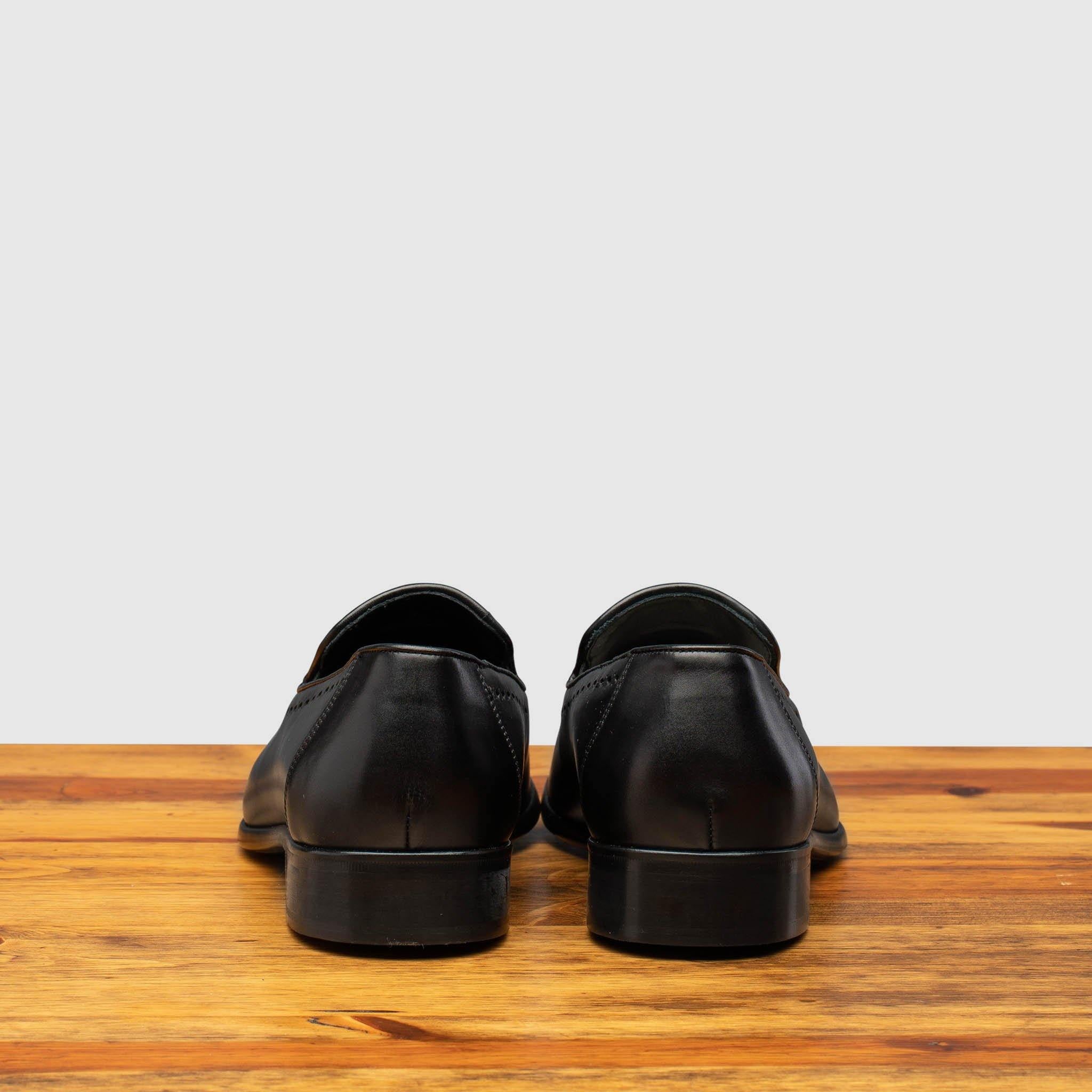Pair of black leather loafer shoe on a wooden surface with a light gray background