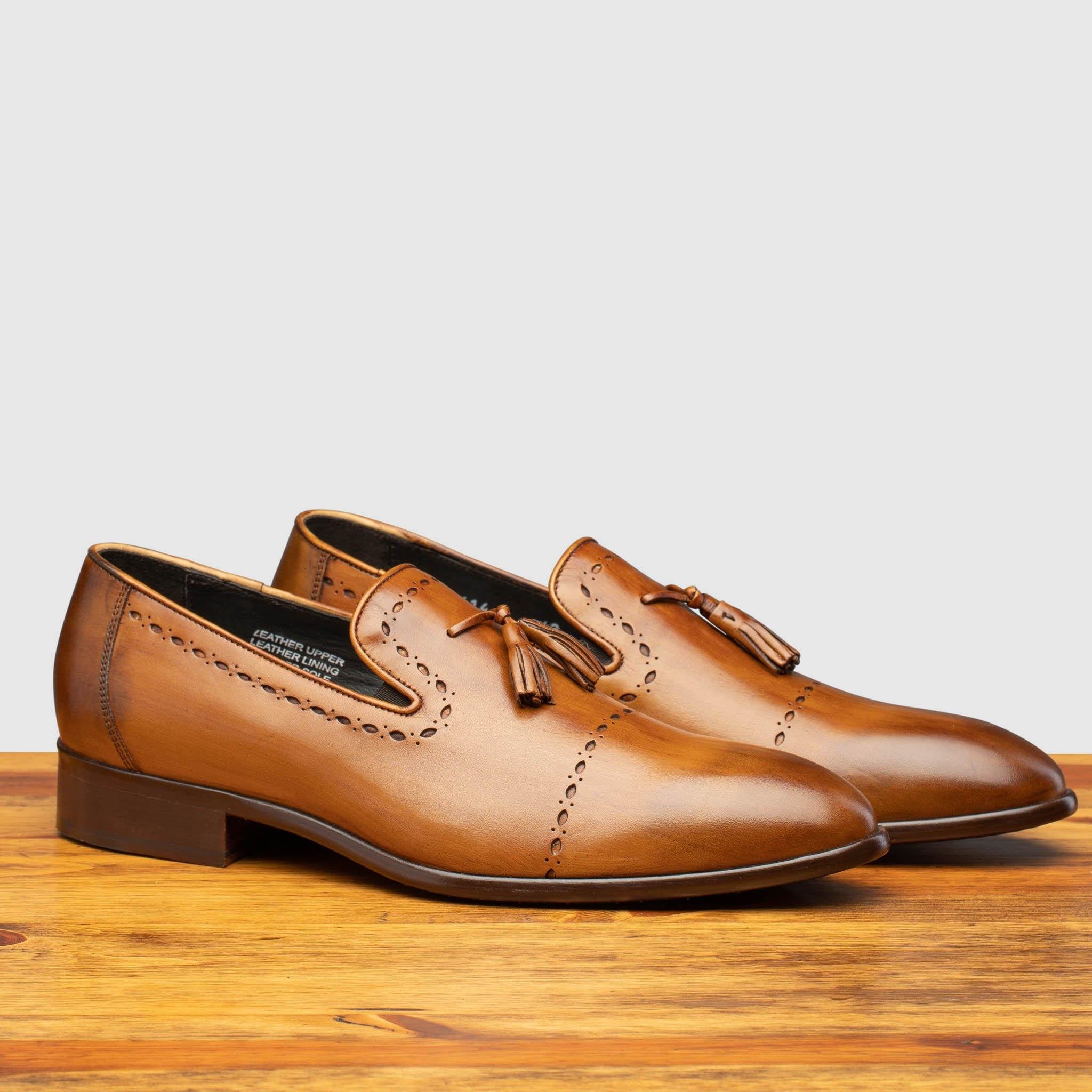 Pair of Chestnut leather loafer shoe on a wooden surface with a light gray background