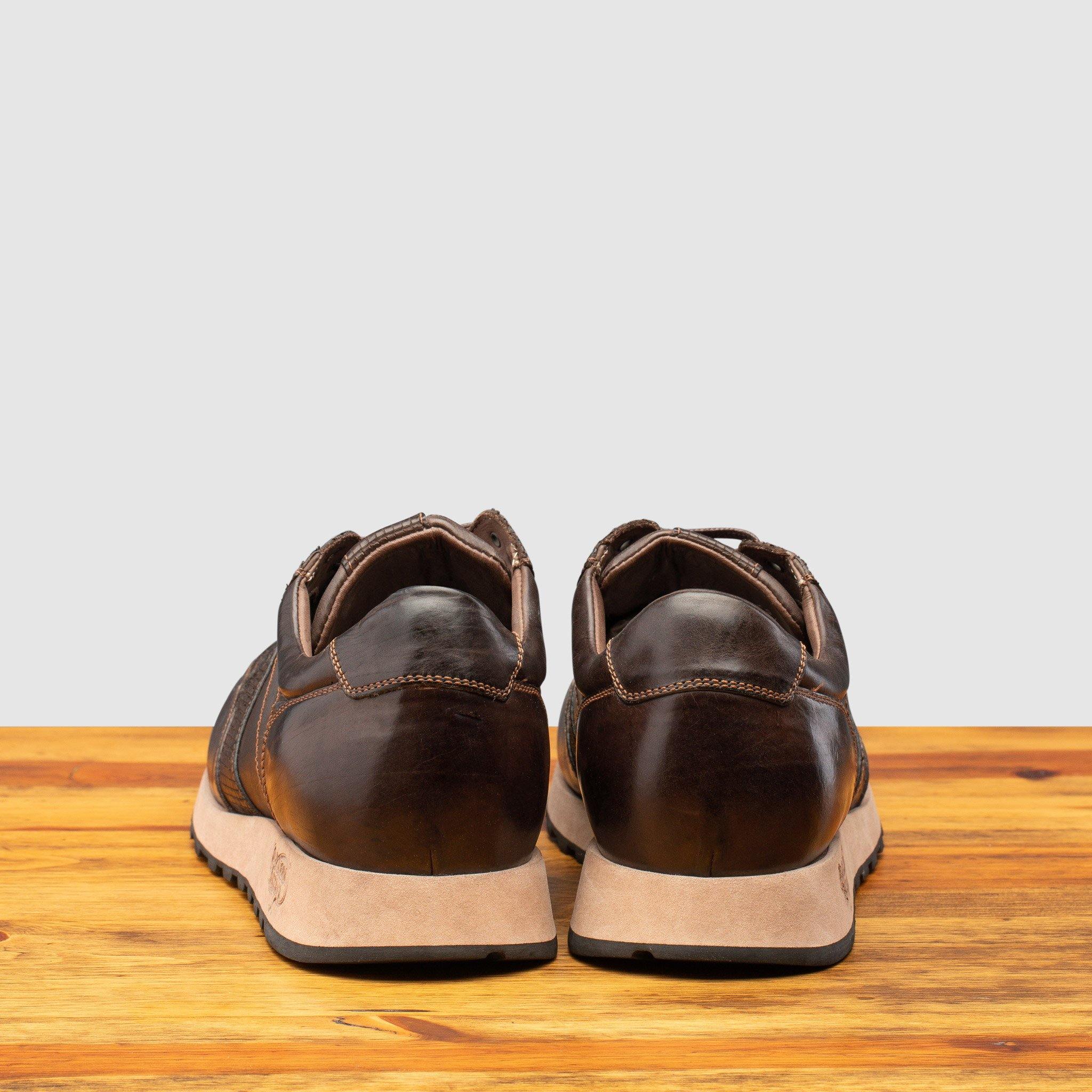 Back side of Brown leather sneaker on a wooden surface with a light gray background