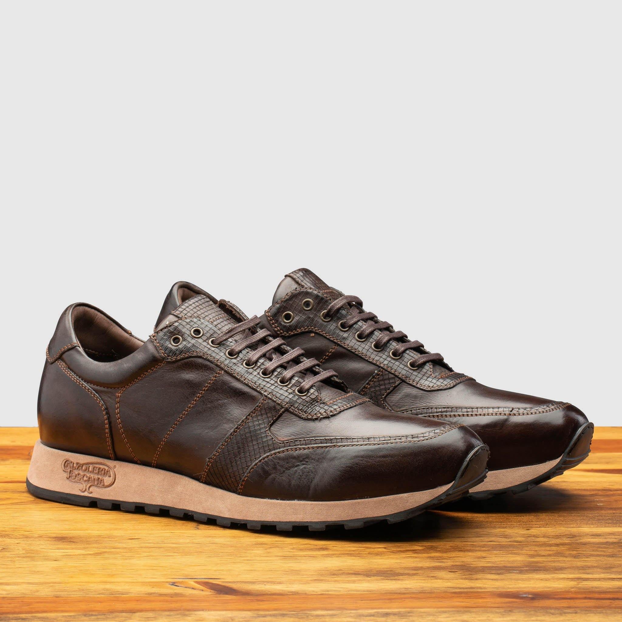 Pair of Brown leather sneaker on a wooden surface with a light gray background