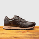 Brown leather sneaker on a wooden surface with a light gray background