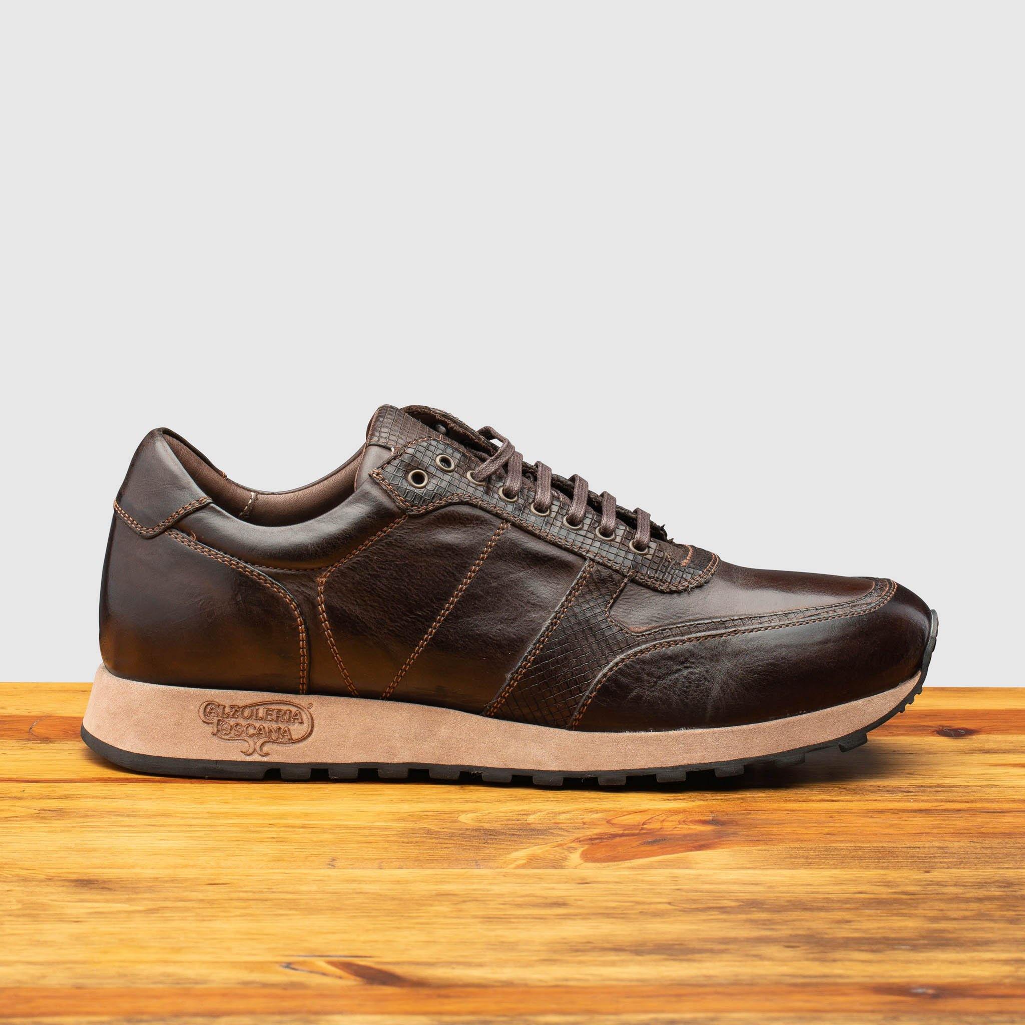 Brown leather sneaker on a wooden surface with a light gray background