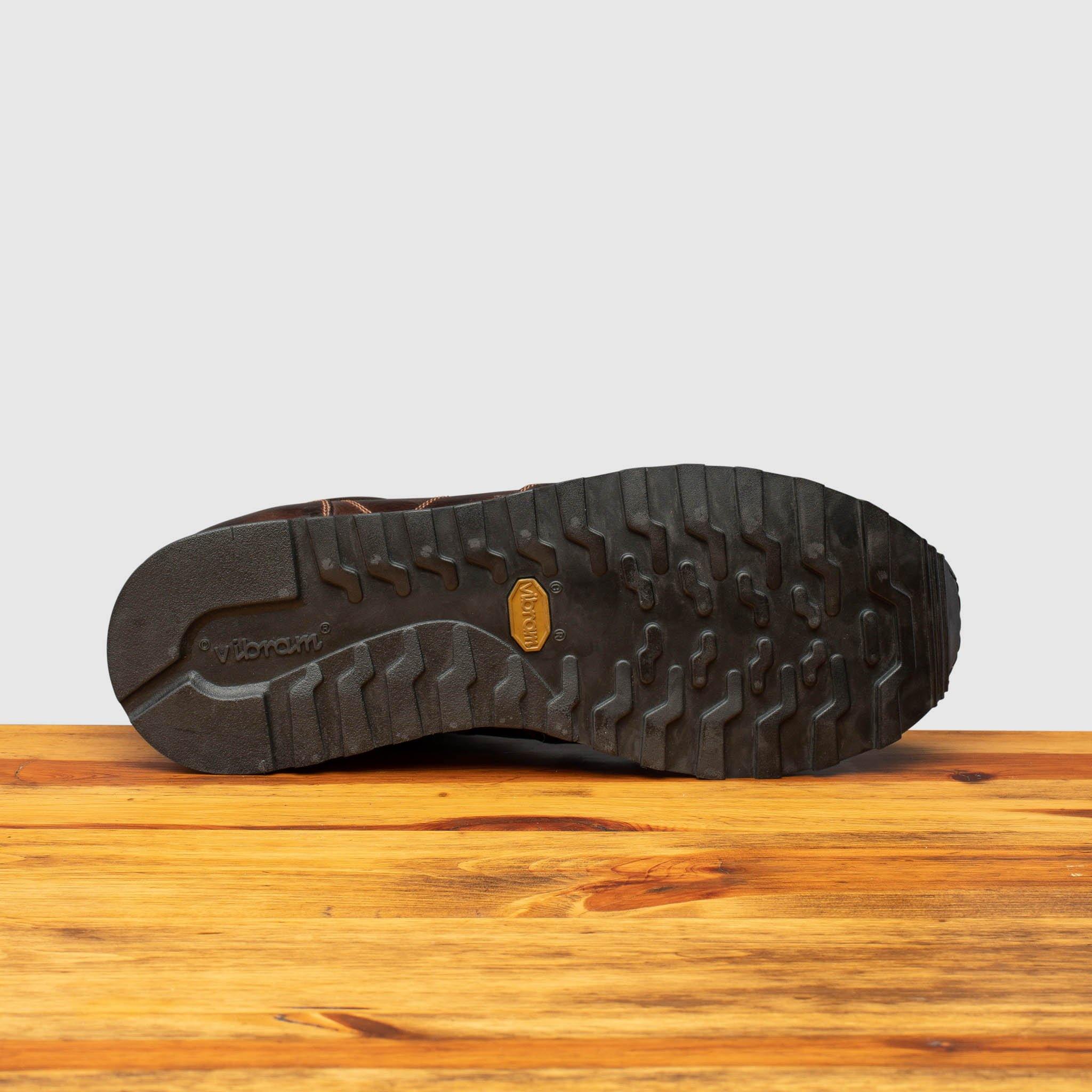 Outsole of Brown leather sneaker on a wooden surface with a light gray background