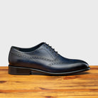 Blue leather dress shoe on a wooden surface with a light gray background