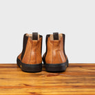 Back view of Brown leather Chelsea boot with black sole on a wooden surface