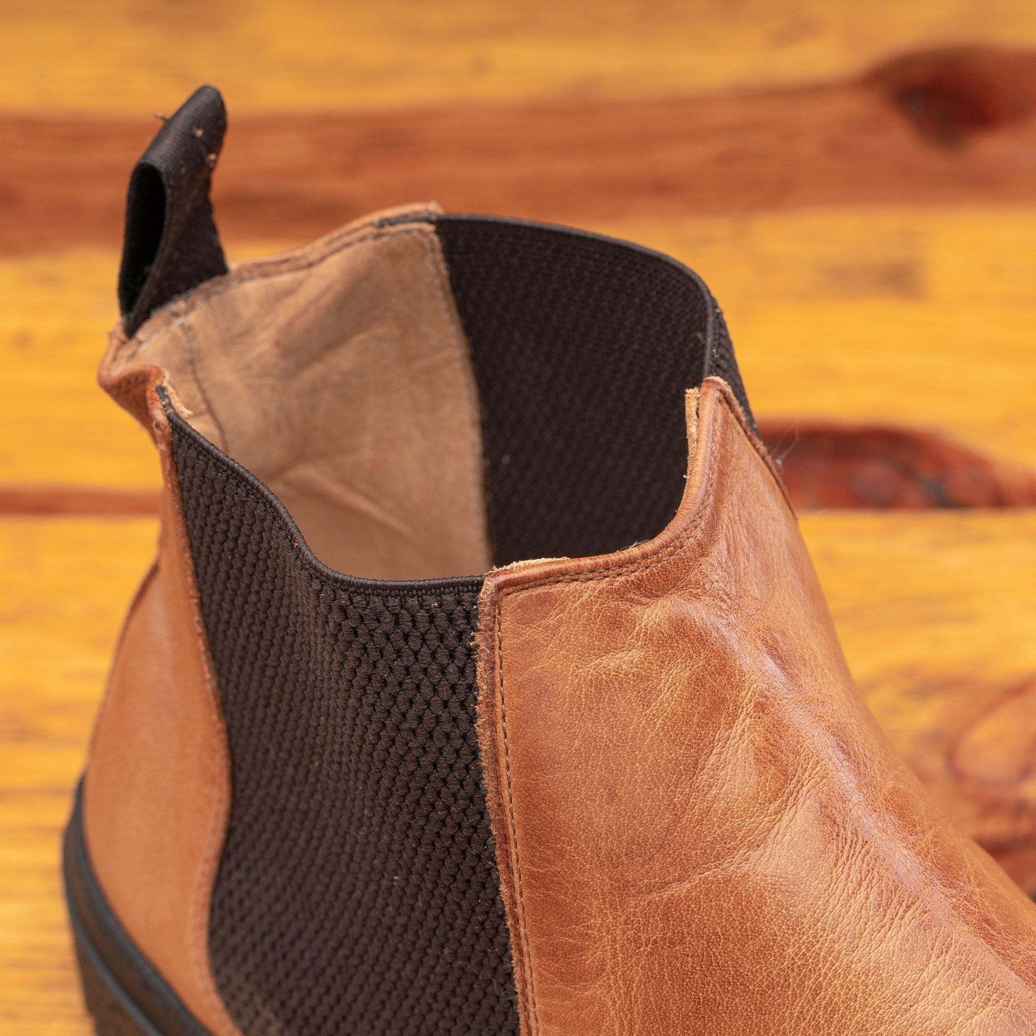 Close view of Brown leather Chelsea boot with black sole on a wooden surface
