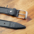 Black leather belt with silver buckle on a wooden surface