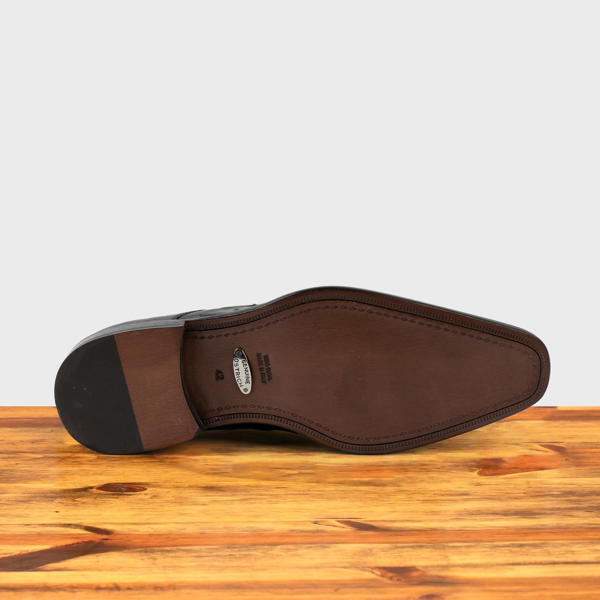 Outsole of Black dress shoe on a wooden surface with a light gray background