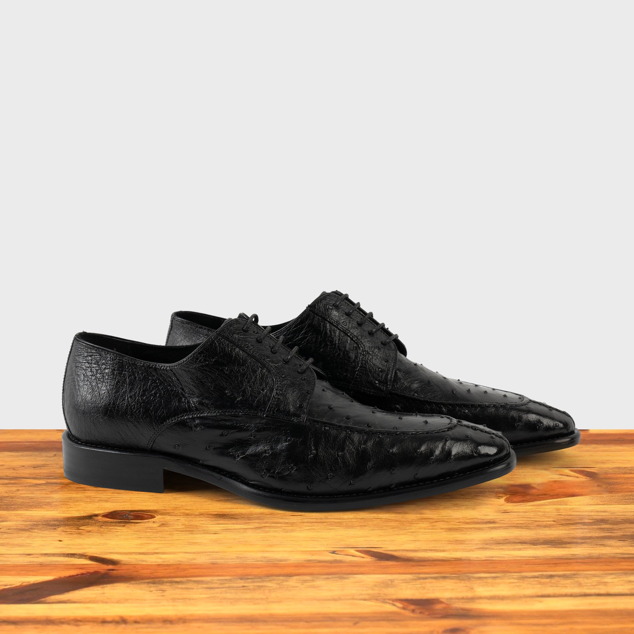 A Pair of Black dress shoe on a wooden surface with a light gray background