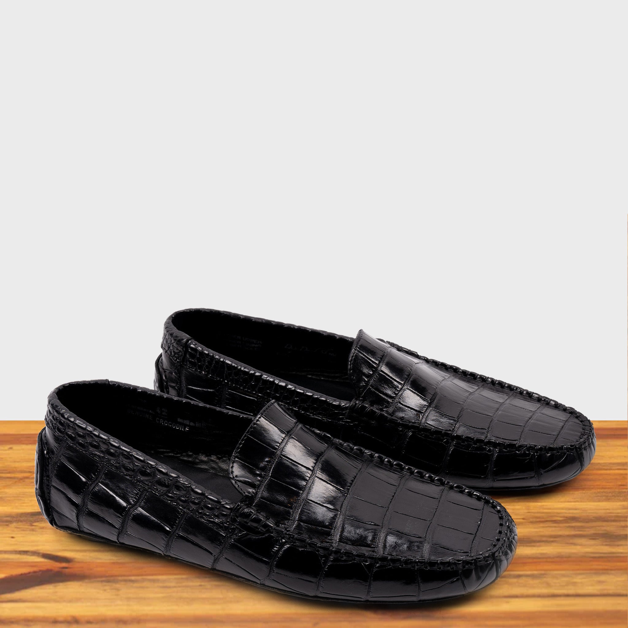 A Pair of Black crocodile-patterned loafer on a wooden surface with a light gray background