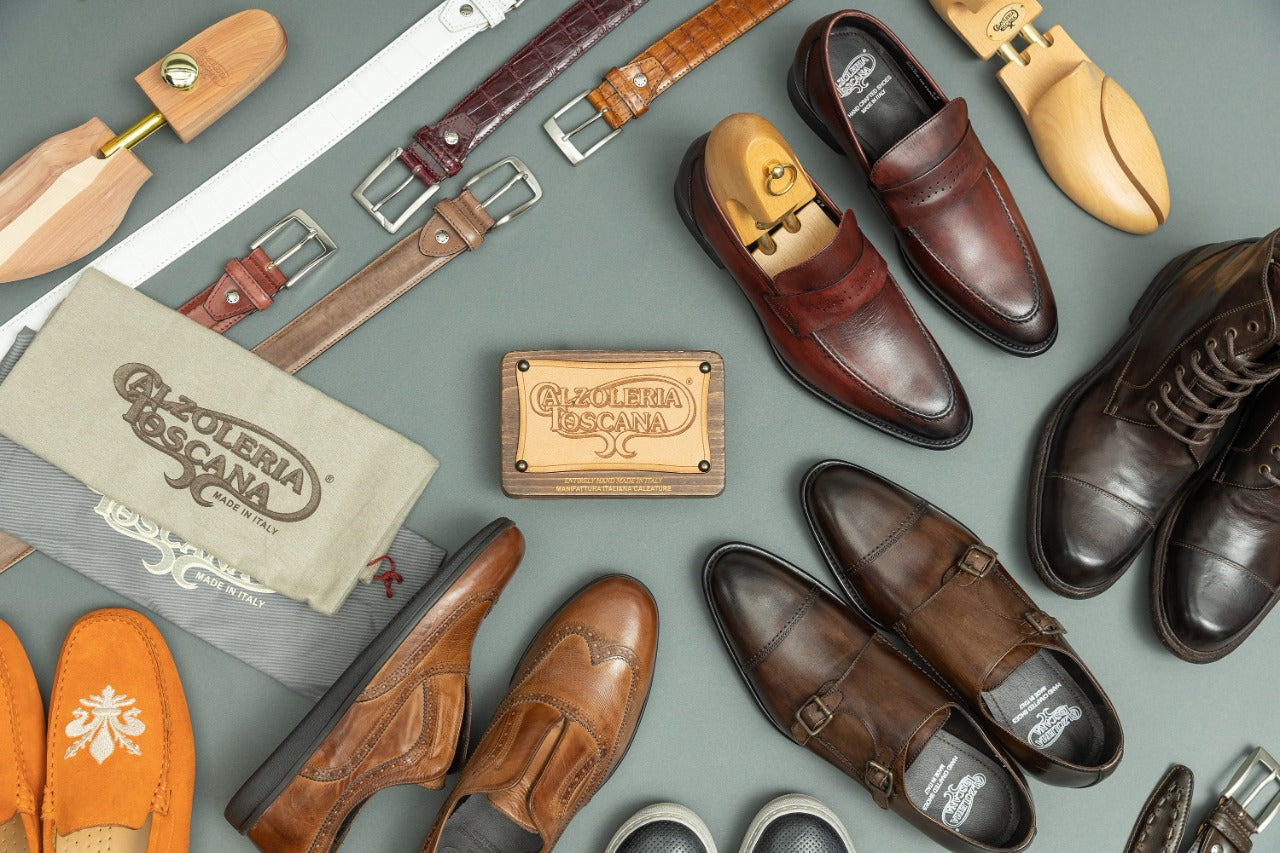 An assortment of brown leather shoes and a wooden box with 'Calzoleria Toscana' branding, indicative of high-quality, hand-made Italian footwear.