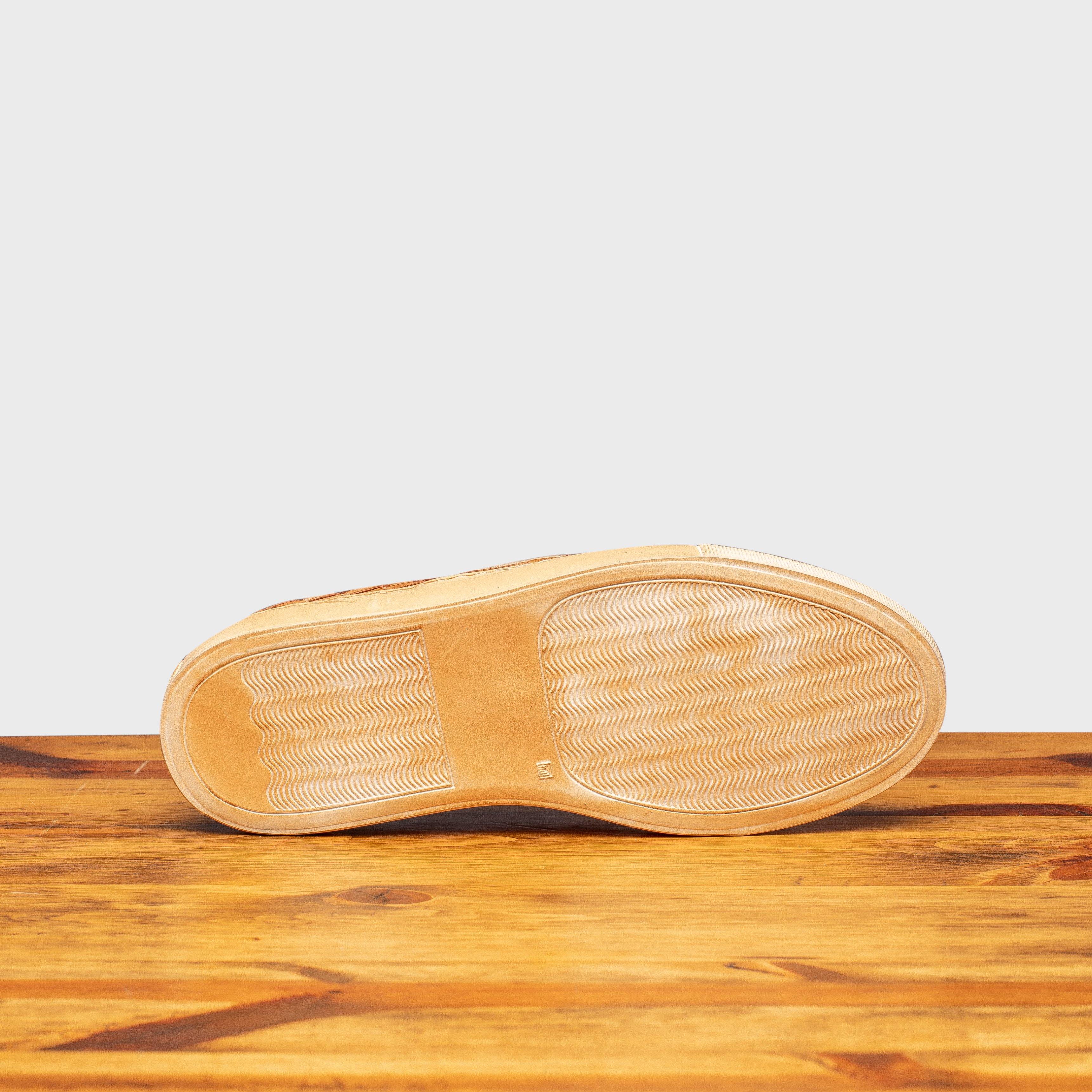 Outsole of woven brown slip-on shoes on a wooden surface